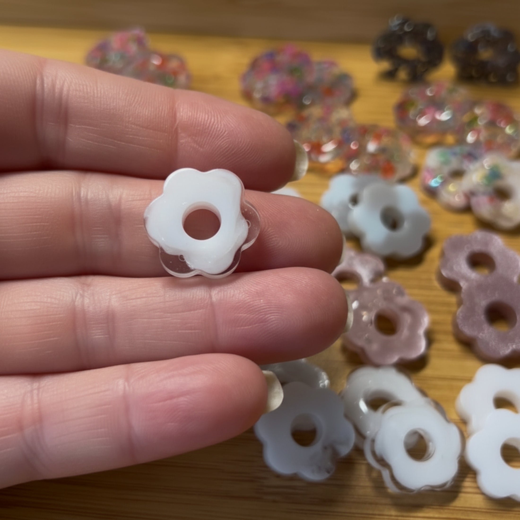 Pampille fleur en résine faite main tenue entre les doigts, diamètre 2 cm, tous coloris disponibles en arrière-plan