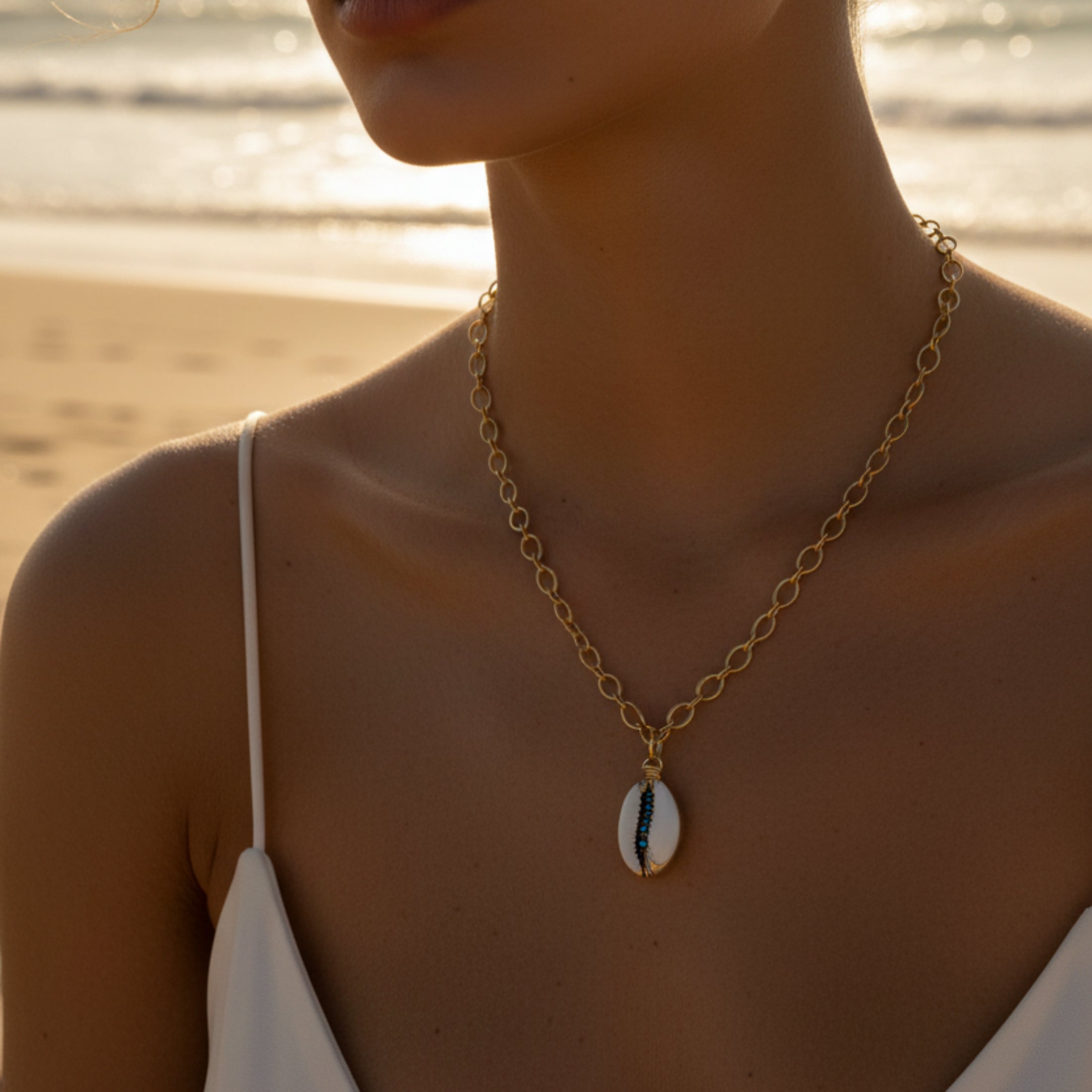 Collier chaîne dorée acier inoxydable, pendentif cauri naturel serti de toupies 2mm bleu nuit, porté au cou.