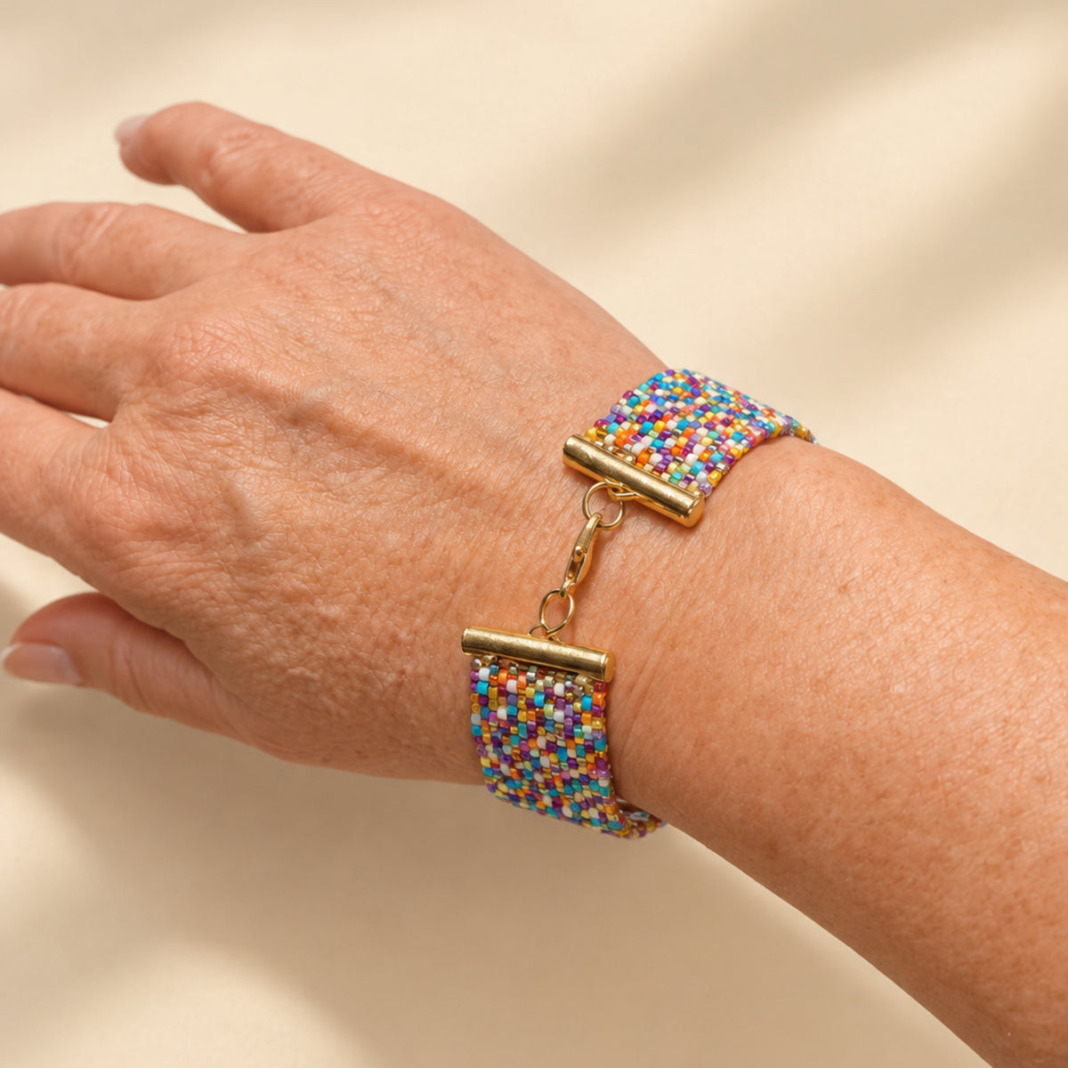 Bracelet Paleta porté au poignet, face mosaïque en perles Miyuki multicolores, avec fermoir en acier inoxydable visible.
