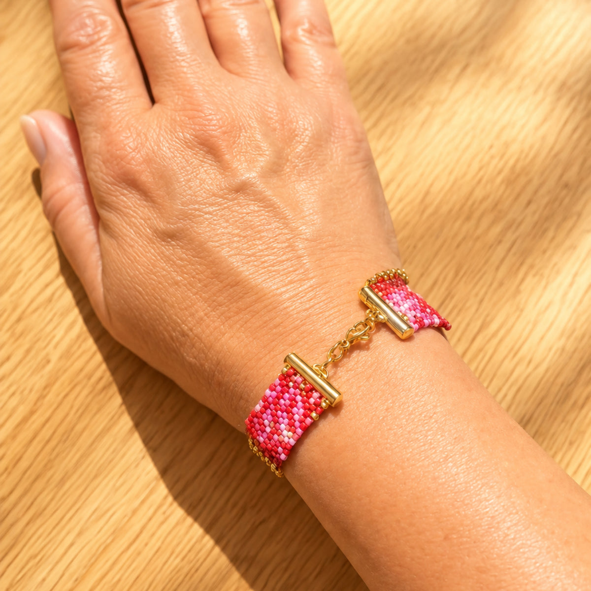 Bracelet Rosalia porté au poignet, côté larges parties tissées à la main en perles Miyuki roses, rouges et dorées, avec fermoir visible.

