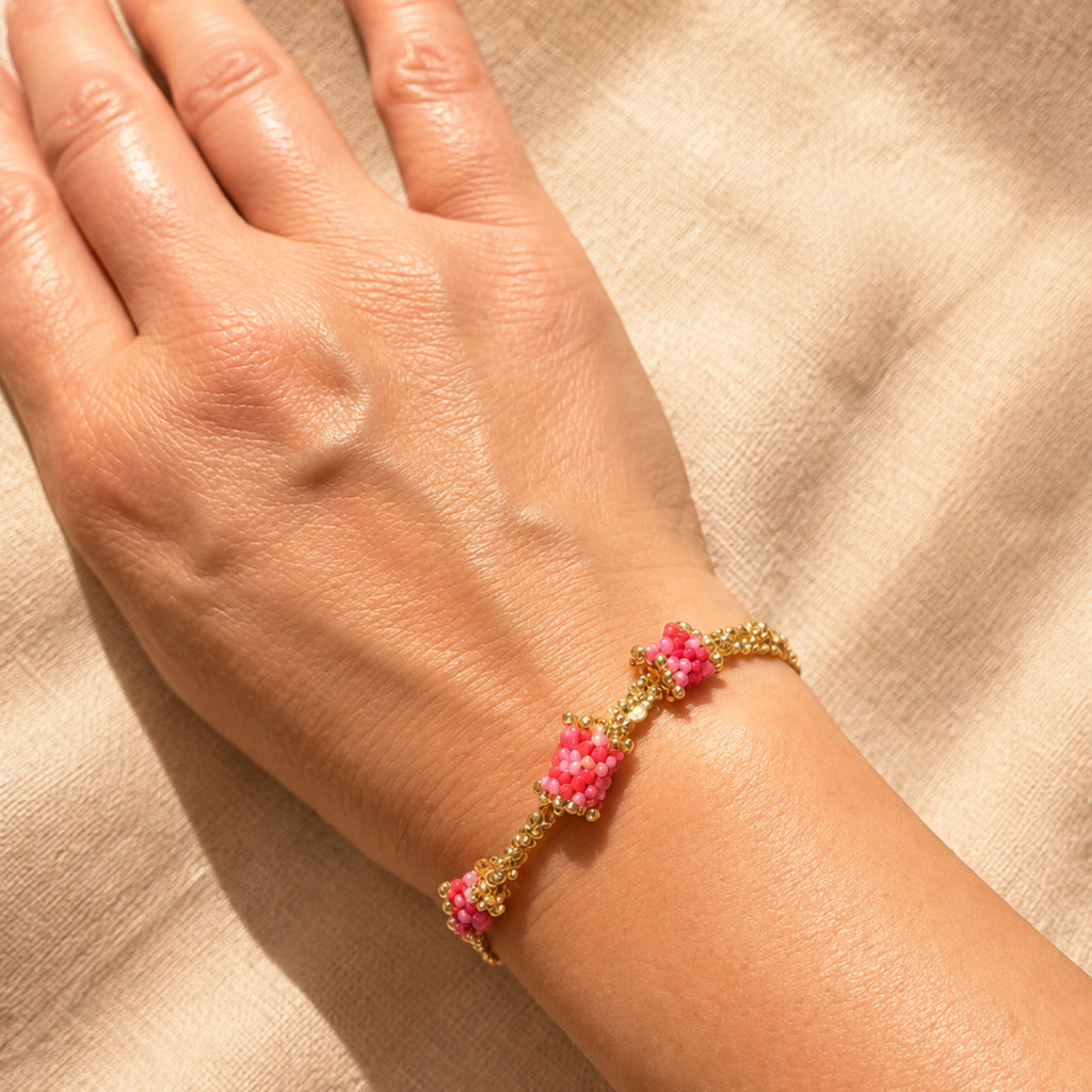 Bracelet Rosalia porté au poignet, éléments tissés en perles Miyuki roses, rouges et dorées coulissant sur des chaînes en acier inoxydable.
