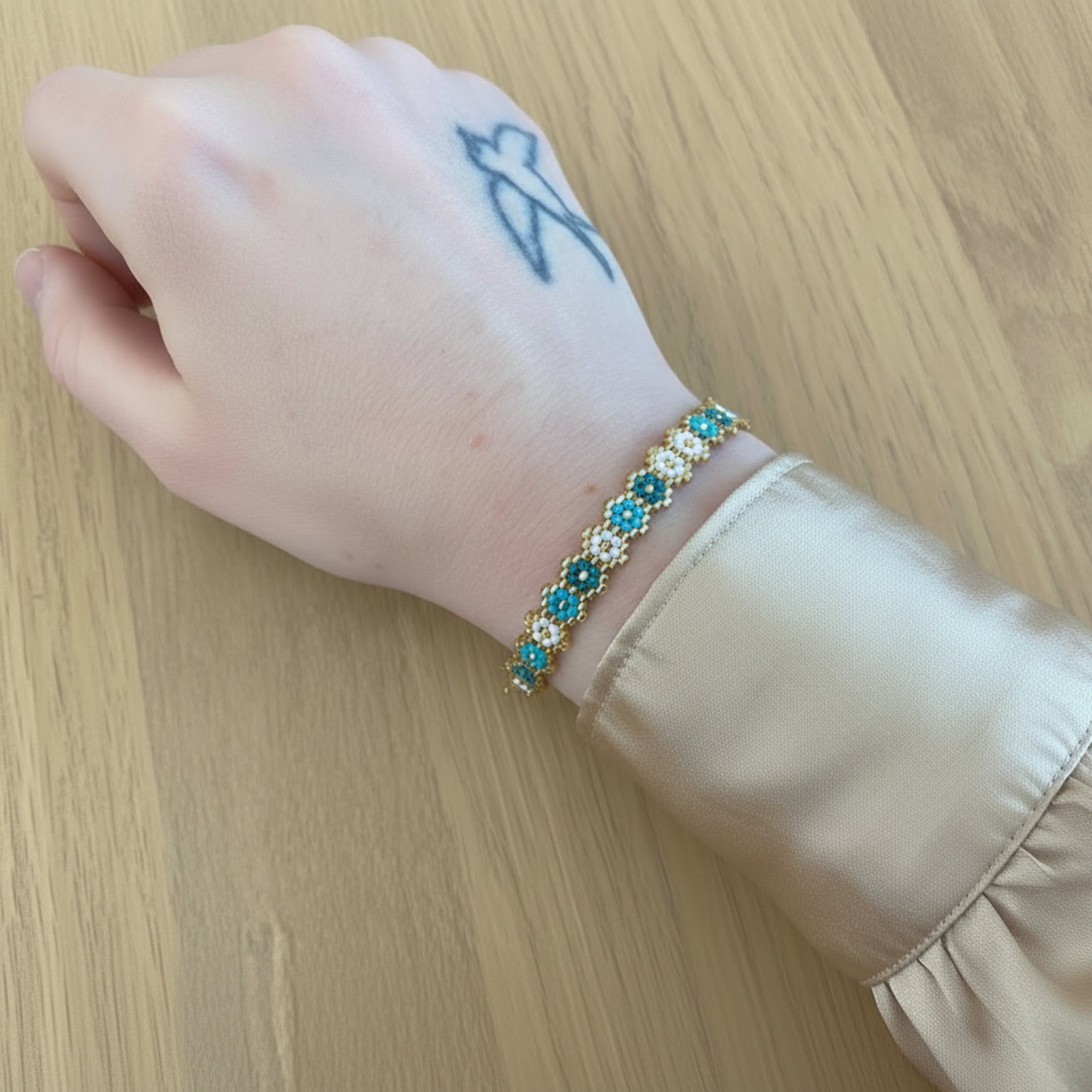 Bracelet fait main Owen ÔParis porté au poignet — perles Miyuki motifs floraux coloris bleu, chaîne acier inoxydable doré